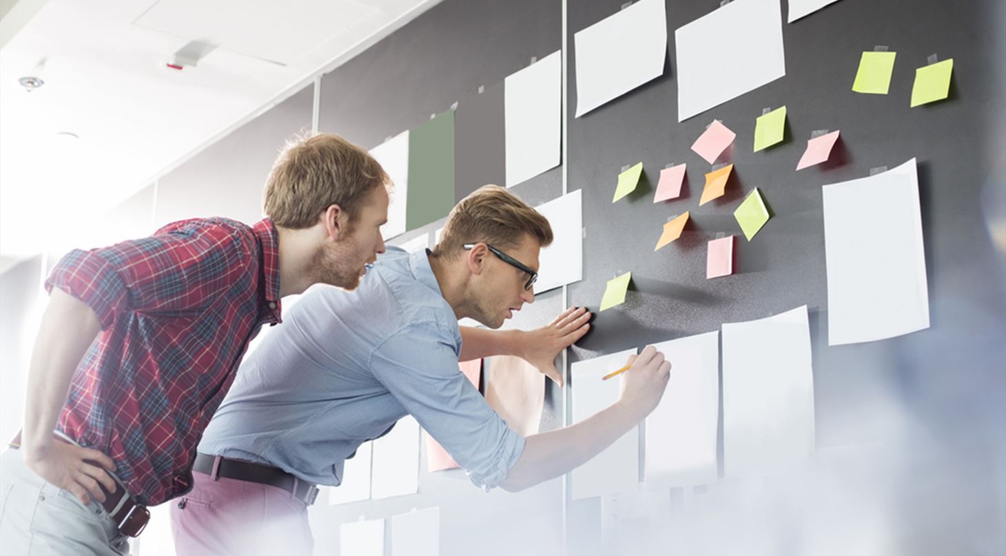 To mænd arbejder med data på tavle med post-its.
